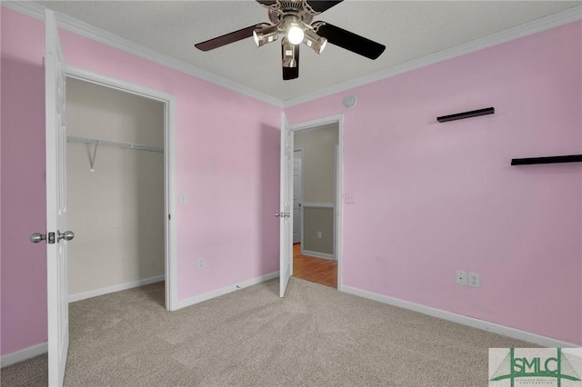 unfurnished bedroom with carpet floors, a ceiling fan, baseboards, ornamental molding, and a closet