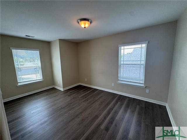 spare room featuring plenty of natural light, dark wood-style flooring, baseboards, and visible vents