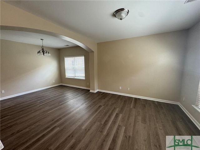 spare room with dark wood-type flooring, arched walkways, baseboards, and an inviting chandelier