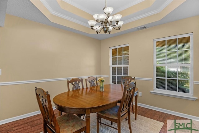 dining space with crown molding, a raised ceiling, wood finished floors, and a notable chandelier