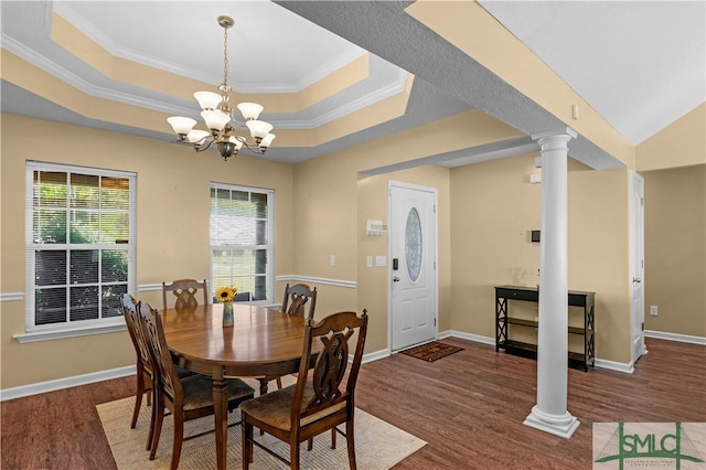 dining room with ornamental molding, decorative columns, wood finished floors, a tray ceiling, and a notable chandelier