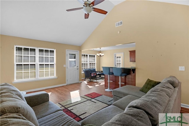 living area with high vaulted ceiling, ceiling fan with notable chandelier, baseboards, wood finished floors, and visible vents