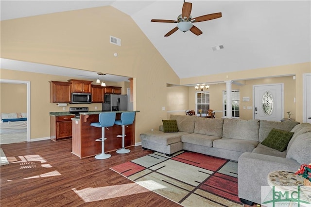 living area with visible vents, dark wood-type flooring, ceiling fan with notable chandelier, and high vaulted ceiling