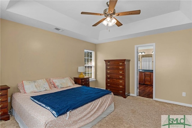 carpeted bedroom with a ceiling fan, visible vents, a raised ceiling, baseboards, and ensuite bathroom
