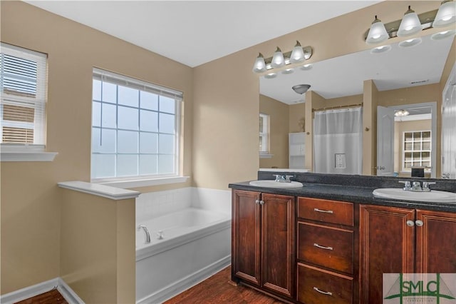full bath featuring a sink, double vanity, a garden tub, and wood finished floors