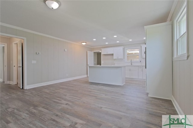 unfurnished living room featuring crown molding, baseboards, a sink, and light wood-style floors