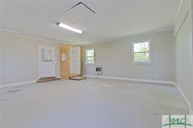 empty room with ornamental molding, heating unit, concrete flooring, baseboards, and attic access