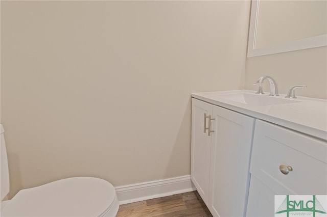 half bath featuring vanity, baseboards, toilet, and wood finished floors