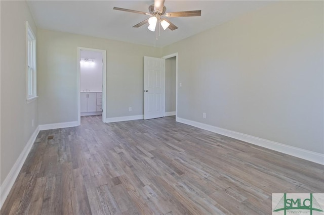 unfurnished bedroom featuring a ceiling fan, baseboards, wood finished floors, and ensuite bathroom