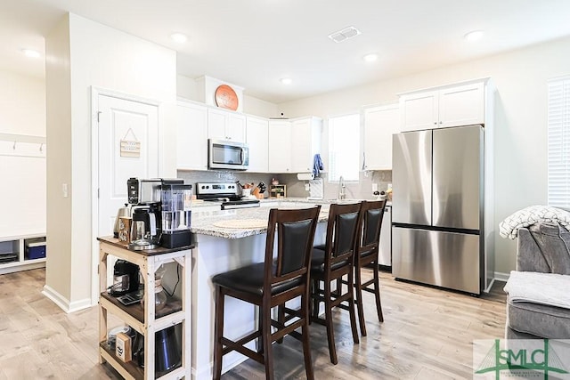 166 Benelli Dr, Pooler, GA 31322 - kitchen with stainless steel appliances, light wood-style floors, white cabinetry, and a kitchen bar