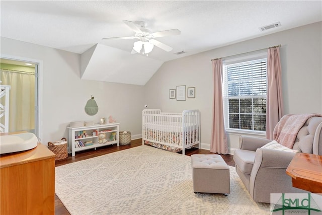 bedroom with visible vents, baseboards, a crib, and wood finished floors