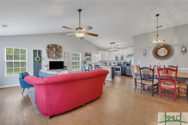 living room with ceiling fan with notable chandelier, vaulted ceiling, light wood-style flooring, and visible vents