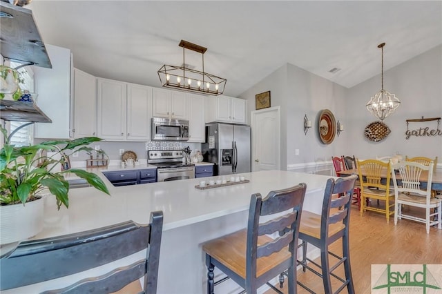 kitchen with a peninsula, light countertops, a chandelier, appliances with stainless steel finishes, and vaulted ceiling