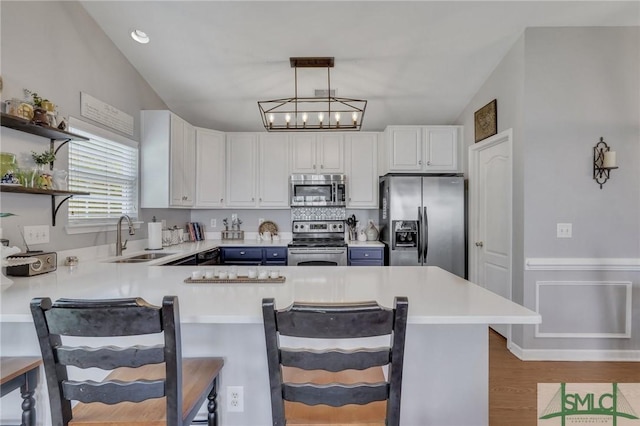 kitchen featuring a sink, a breakfast bar area, stainless steel appliances, a peninsula, and wood finished floors
