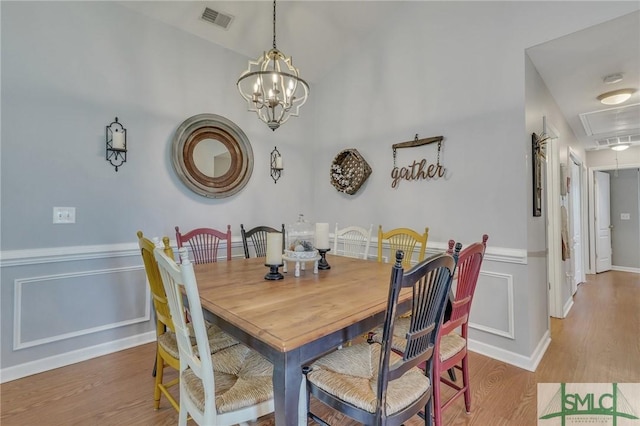 dining room with visible vents, wood finished floors, attic access, a wainscoted wall, and a chandelier