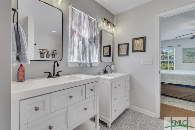 bathroom featuring baseboards, two vanities, a sink, and ensuite bathroom
