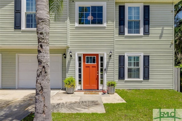 doorway to property featuring an attached garage, a lawn, and concrete driveway
