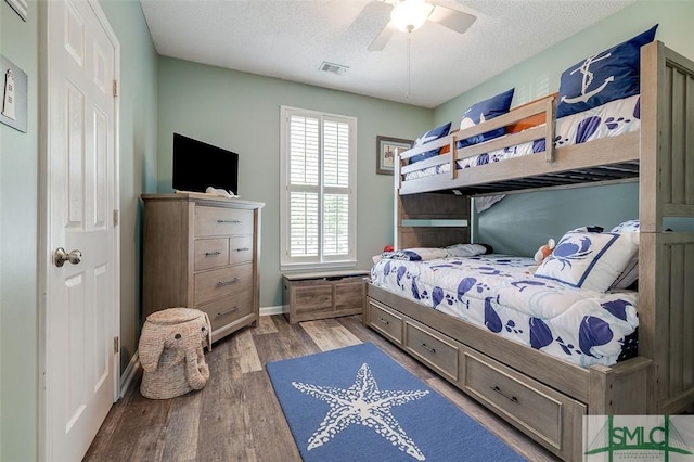bedroom featuring ceiling fan, a textured ceiling, baseboards, wood finished floors, and visible vents