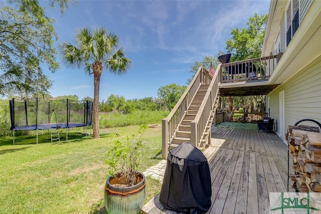 wooden deck with stairs, a yard, a trampoline, and a grill