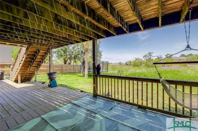 wooden deck featuring a lawn, a fenced backyard, a trampoline, and stairway