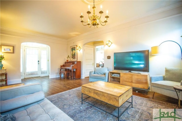 living area featuring crown molding, arched walkways, wood finished floors, baseboards, and an inviting chandelier