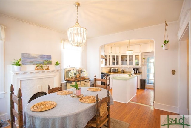 dining area with arched walkways, ornamental molding, a healthy amount of sunlight, and light wood-type flooring