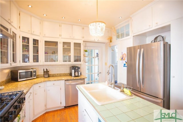 kitchen featuring glass insert cabinets, white cabinetry, a sink, a notable chandelier, and stainless steel appliances