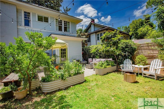 back of house with a lawn, fence, outdoor lounge area, and a vegetable garden