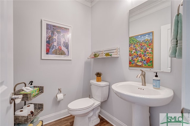 half bathroom with crown molding, baseboards, wood finished floors, and toilet
