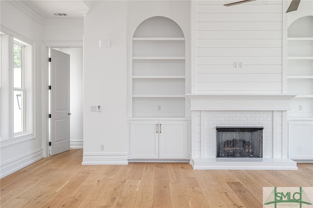 unfurnished living room with visible vents, built in shelves, and light wood-style floors