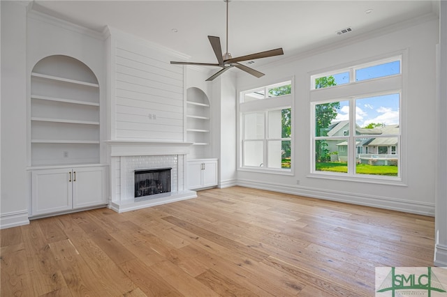 unfurnished living room featuring ceiling fan, ornamental molding, built in shelves, and light wood-style flooring