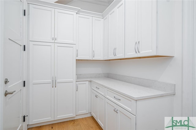 kitchen with light stone counters, light wood-type flooring, and white cabinetry