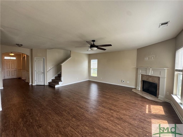unfurnished living room with ceiling fan, visible vents, a high end fireplace, arched walkways, and dark wood-style floors