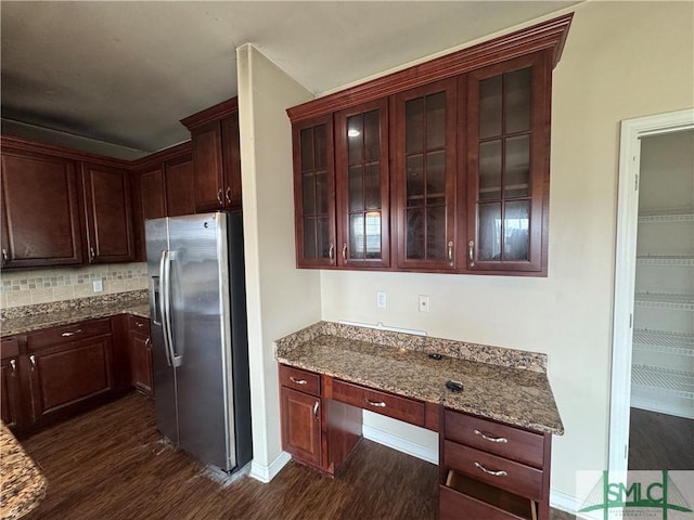 kitchen with built in study area, stone counters, dark wood-style flooring, and stainless steel refrigerator with ice dispenser