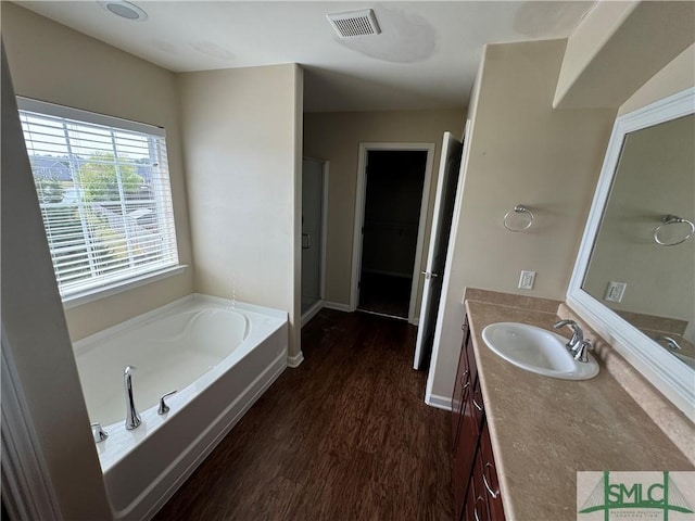 full bath with a garden tub, visible vents, wood finished floors, vanity, and baseboards