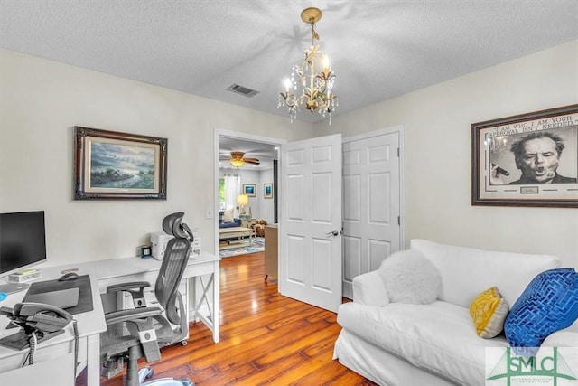home office with a textured ceiling, a notable chandelier, wood finished floors, and visible vents
