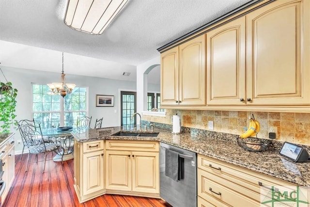 kitchen featuring cream cabinets, a sink, light wood finished floors, dishwasher, and dark stone counters