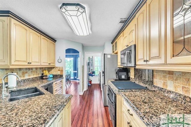 kitchen featuring a sink, appliances with stainless steel finishes, dark stone counters, and glass insert cabinets