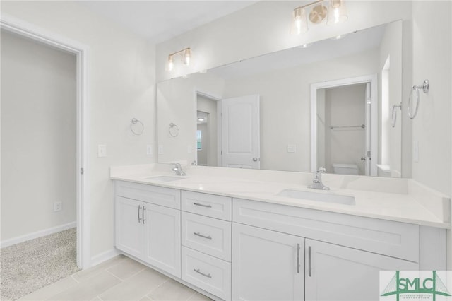 bathroom with baseboards, double vanity, toilet, and a sink