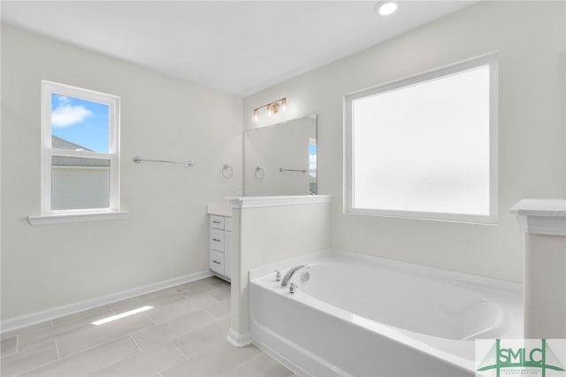 full bath featuring vanity, baseboards, a bath, and a wealth of natural light