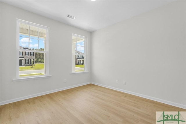 unfurnished room featuring a healthy amount of sunlight, baseboards, light wood-type flooring, and visible vents