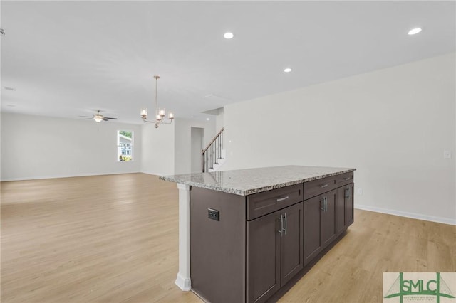 kitchen with dark brown cabinetry, light wood-style floors, ceiling fan with notable chandelier, a center island, and open floor plan