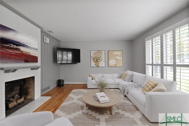 living room with visible vents, a fireplace with raised hearth, wood finished floors, and a healthy amount of sunlight