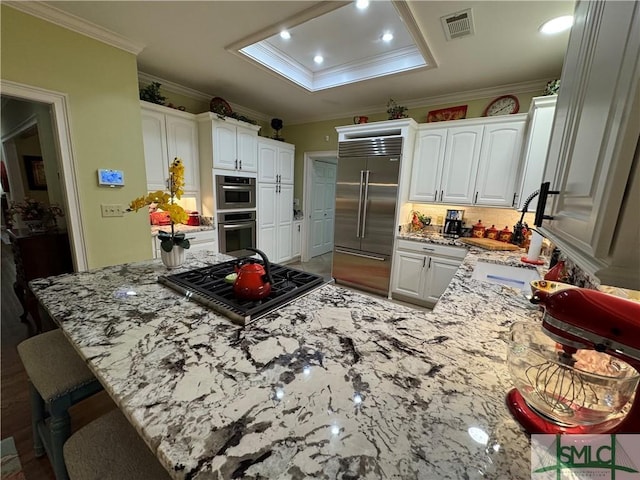 kitchen with a peninsula, stainless steel appliances, white cabinets, crown molding, and light stone counters