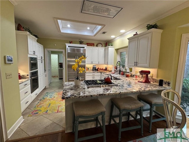 kitchen with a peninsula, a breakfast bar area, appliances with stainless steel finishes, light stone counters, and ornamental molding