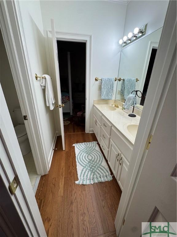 bathroom featuring double vanity, toilet, wood finished floors, a sink, and baseboards