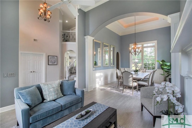 living area with crown molding, arched walkways, baseboards, wood finished floors, and visible vents