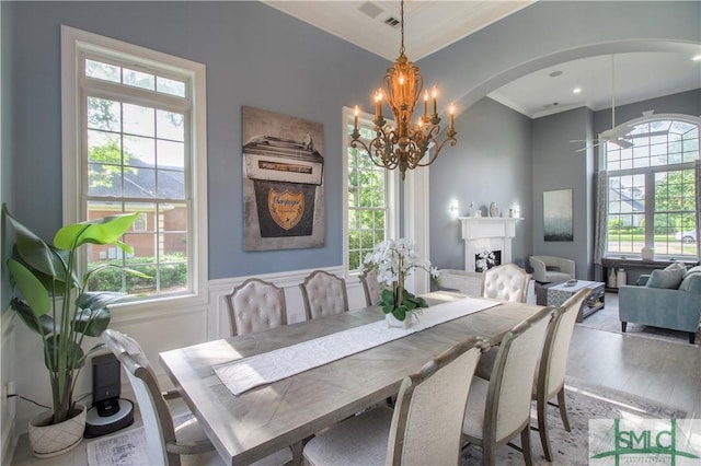 dining area with an inviting chandelier, arched walkways, crown molding, and wood finished floors