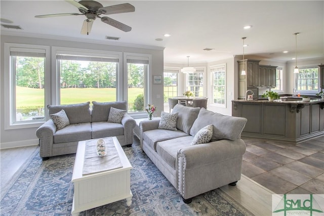 living area featuring baseboards, ornamental molding, ceiling fan, and visible vents