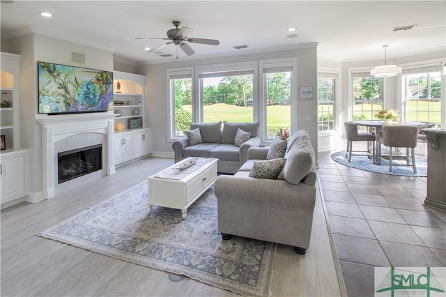living area with a ceiling fan, visible vents, plenty of natural light, and ornamental molding